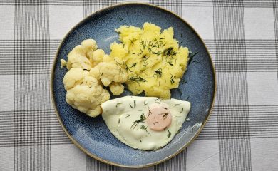 Danie obiadowe na granatowym talerzu: jajko sadzone, gotowany kalafior i puree ziemniaczane posypane koperkiem.