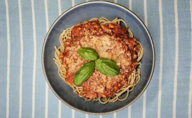Spaghetti pełnoziarniste z gęstym sosem bolognese i parmezanem, udekorowane świeżymi listkami bazylii.